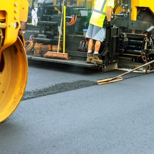 Road roller at a road construction site, paver laying fresh asphalt pavement during road