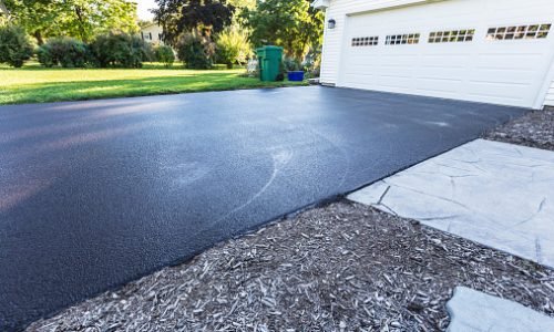 A fresh blacktop resealing job just finished on this asphalt driveway in a suburban residential district.